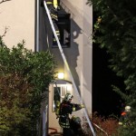 Ein Trupp beim kühlt das Dach eines Mehrfamilienhauses nach einem Wohnungsbrand